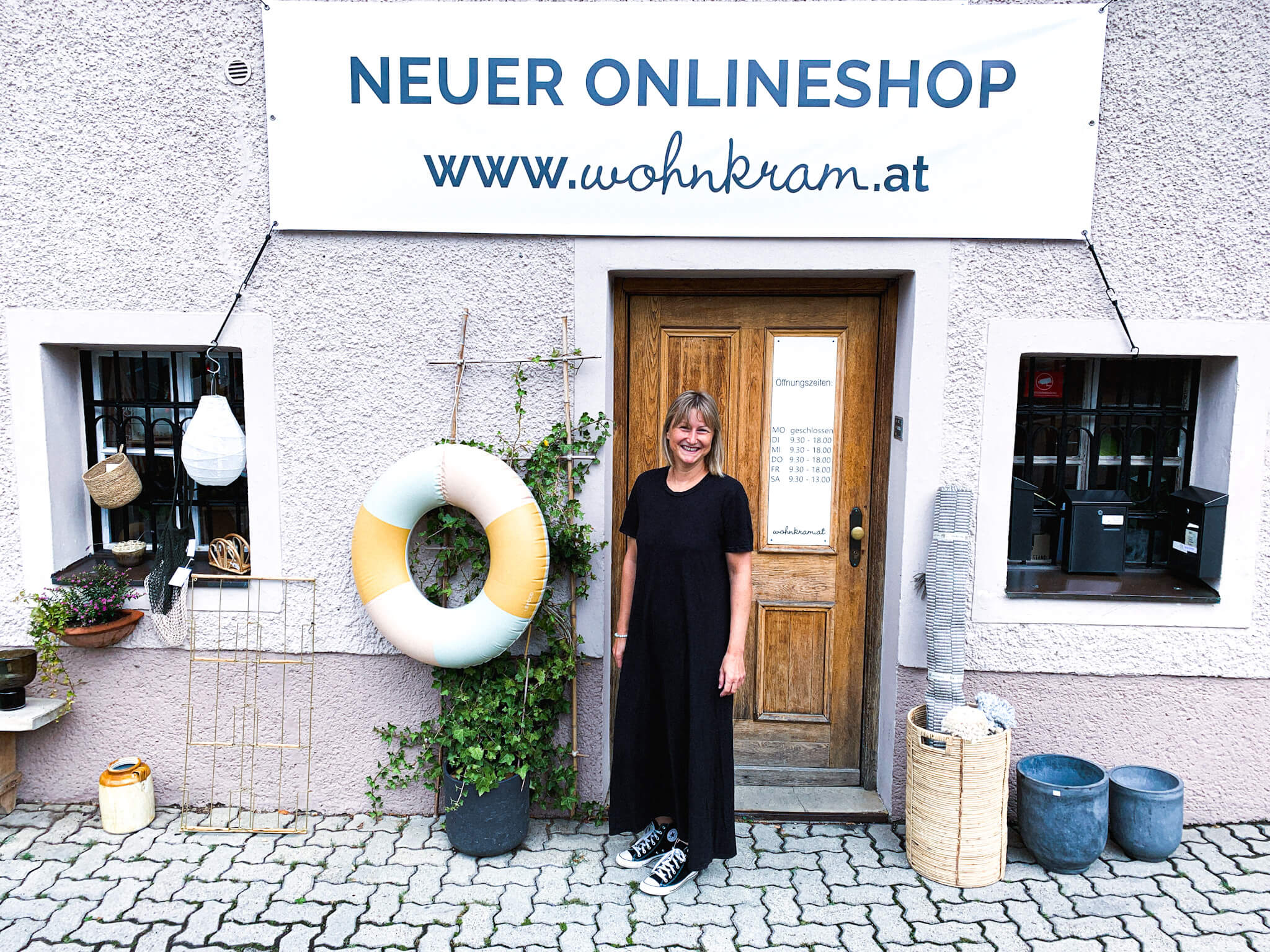 Frau vor Laden mit dem Schild "Neuer Onlineshop www.wohnkram.at"