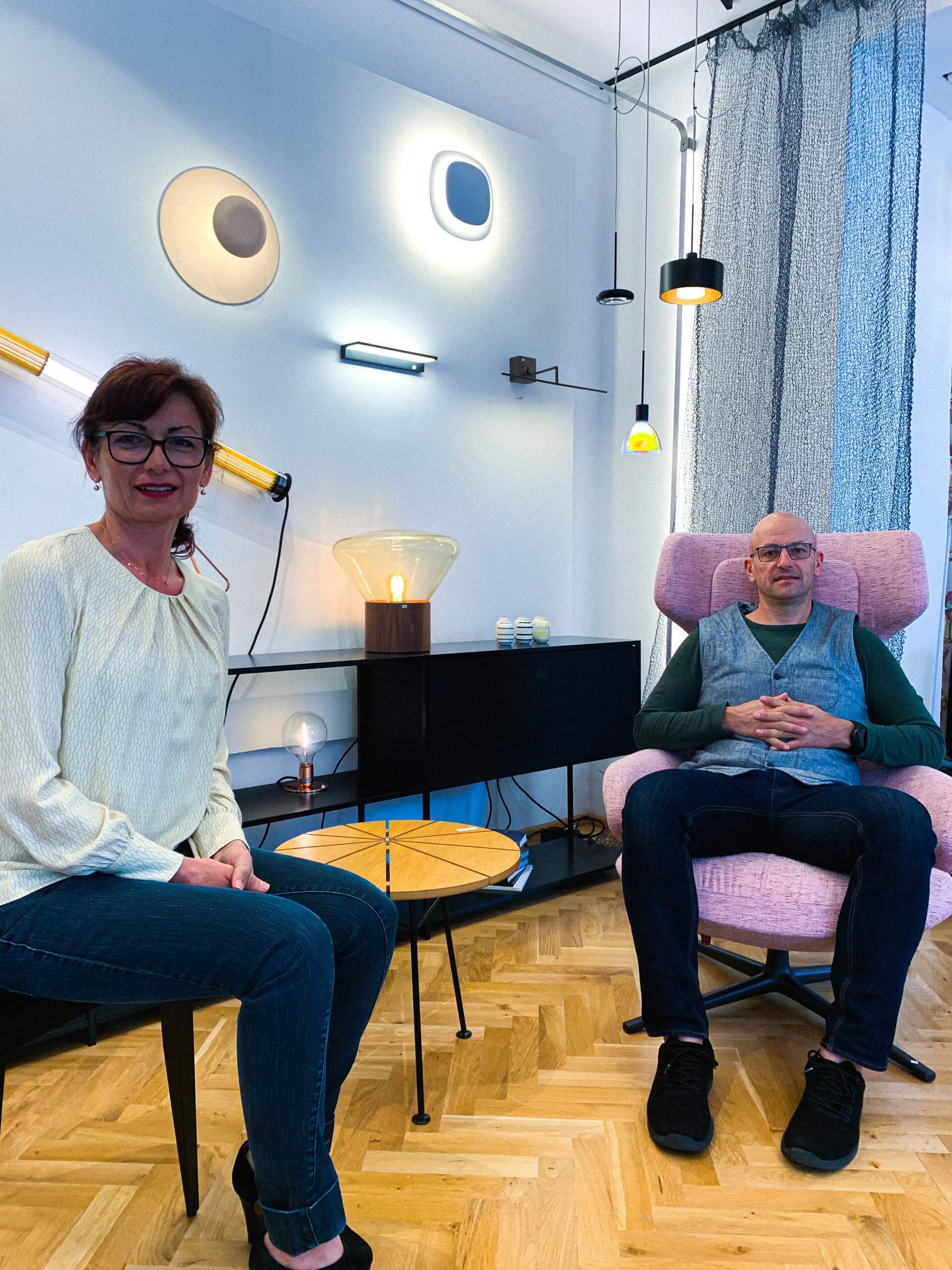 Eine Frau und ein Mann sitzen in modern eingerichtetem Wohnzimmer mit bunten Möbeln und kunstvoller Deckenleuchte