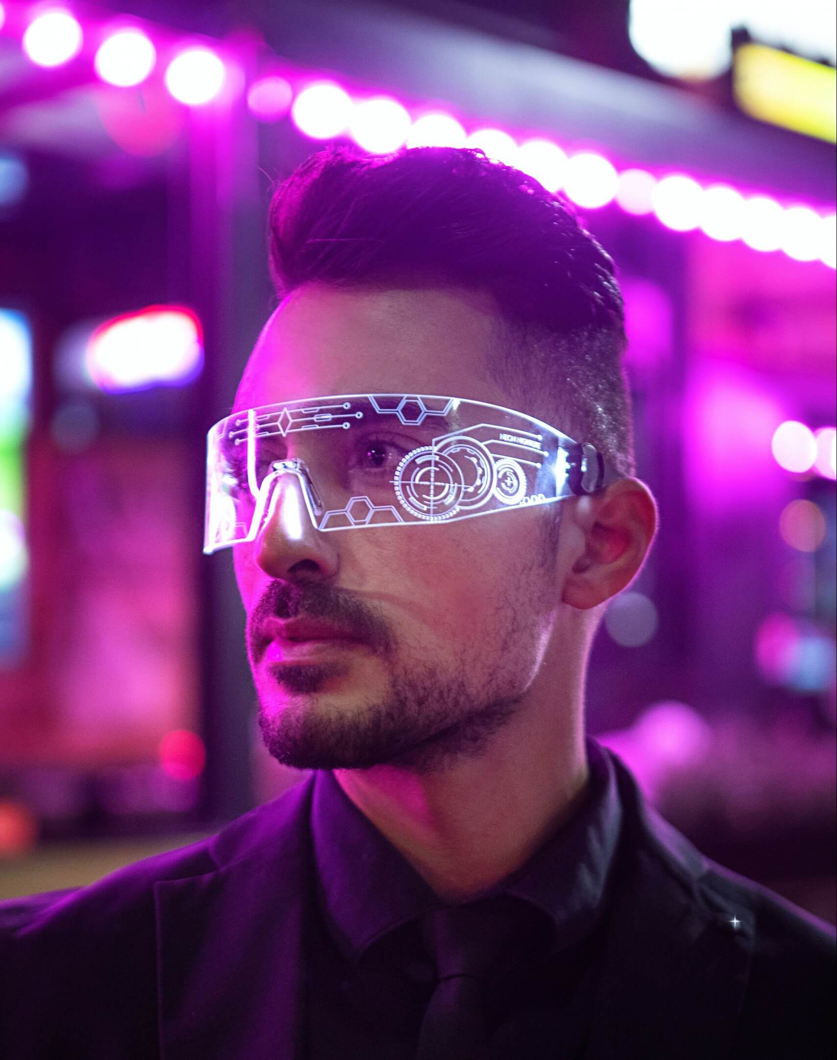Ein Mann der von lila Lichtern angeleuchtet wird und eine futuristische Brille trägt